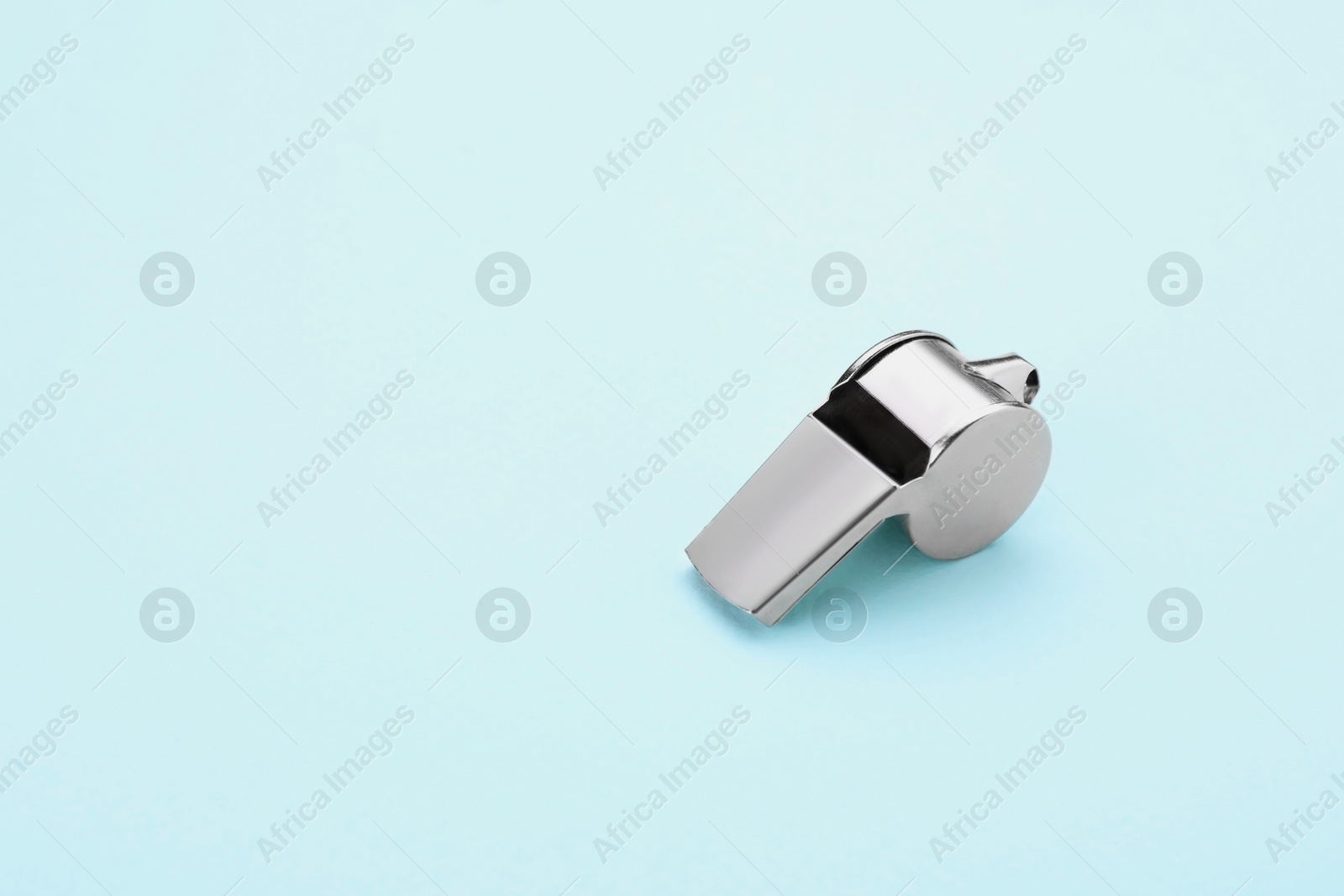 Photo of One metal whistle on light blue background, space for text
