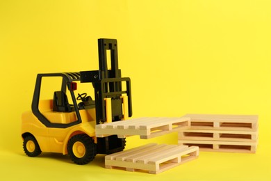 Photo of Toy forklift and wooden pallets on yellow background
