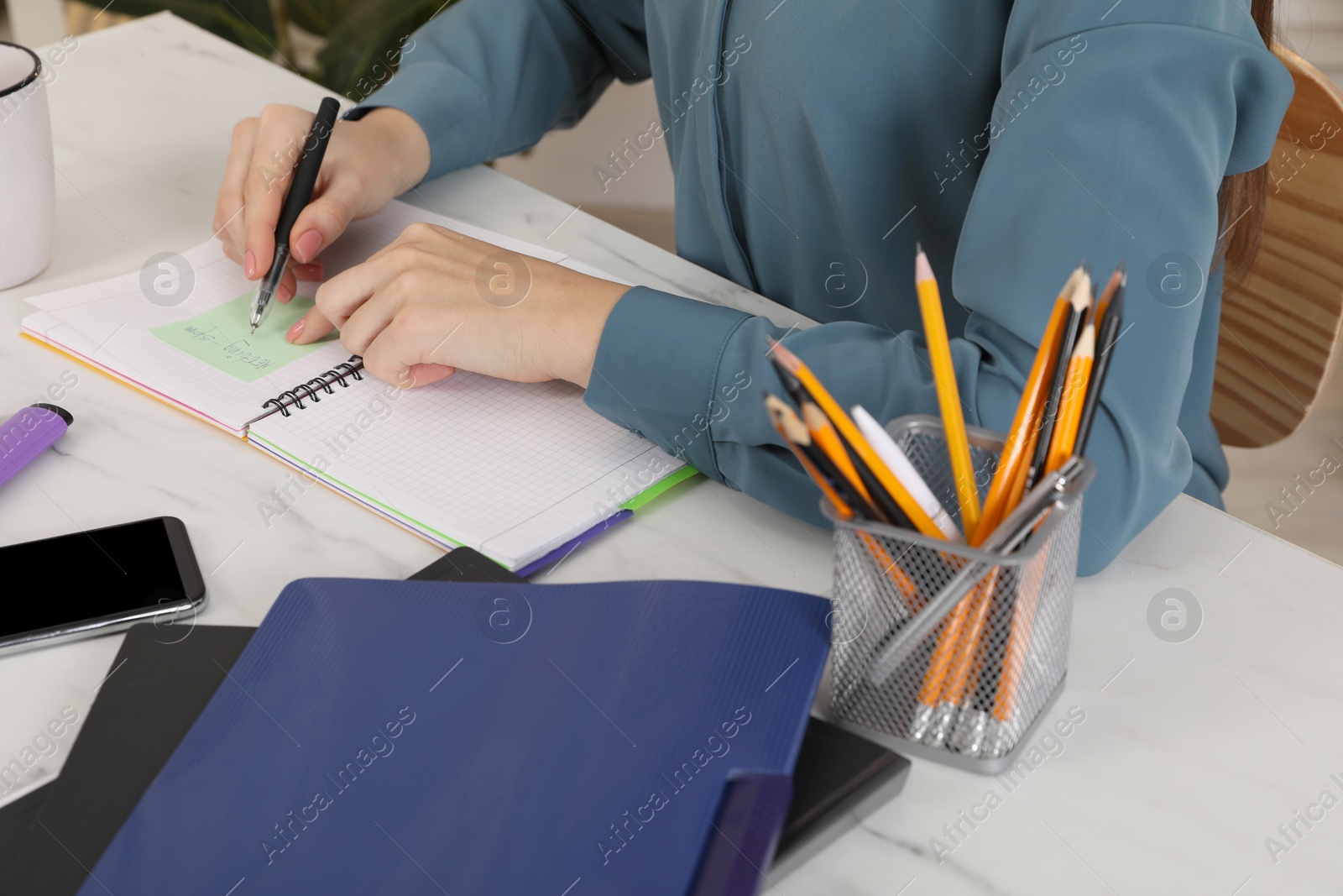 Photo of Woman writing on sticky note at white marble table indoors, closeup