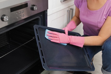 Photo of Woman cleaning oven tray with rag in kitchen, closeup