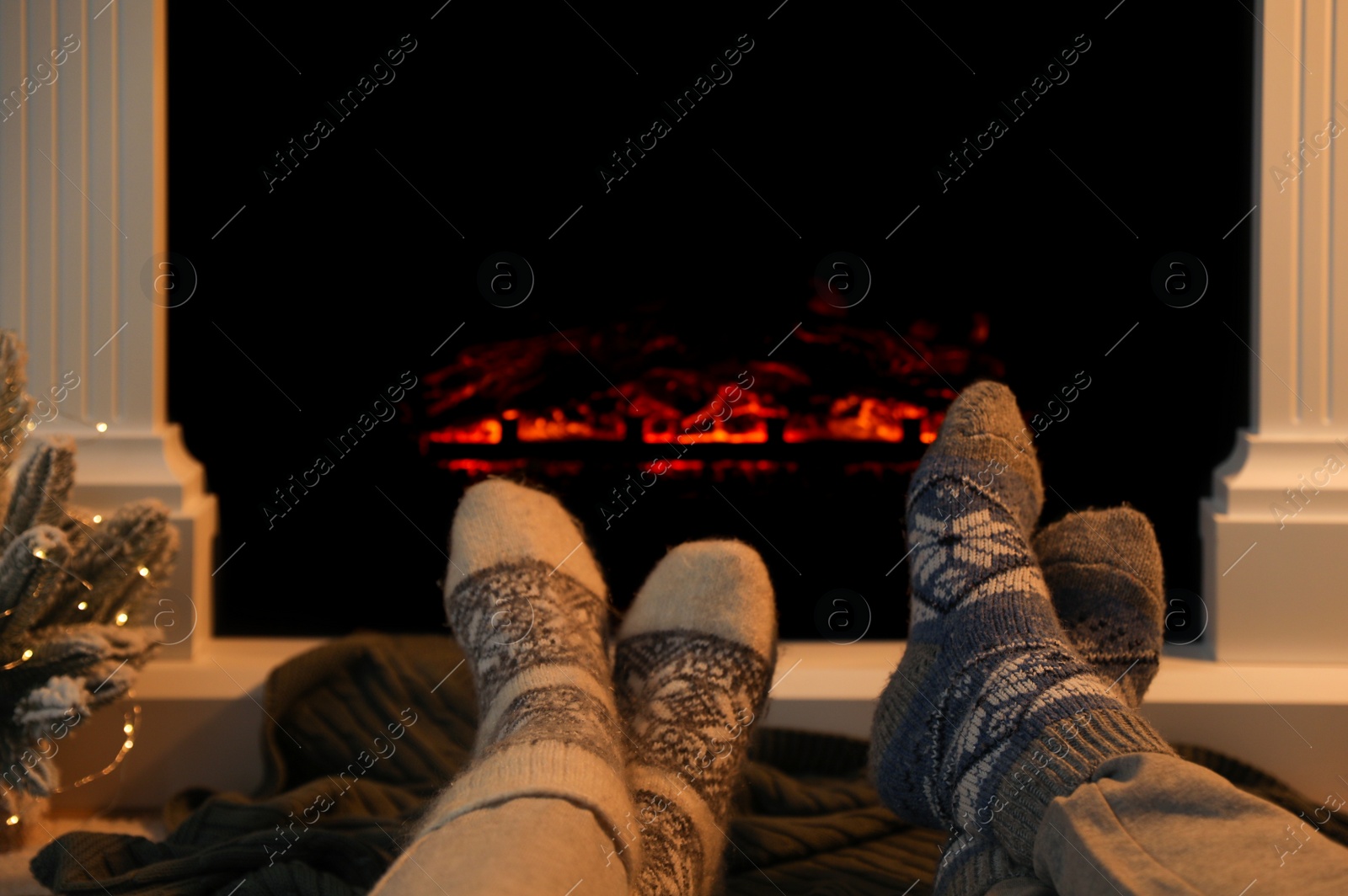 Photo of Couple in warm socks resting near fireplace at home, closeup