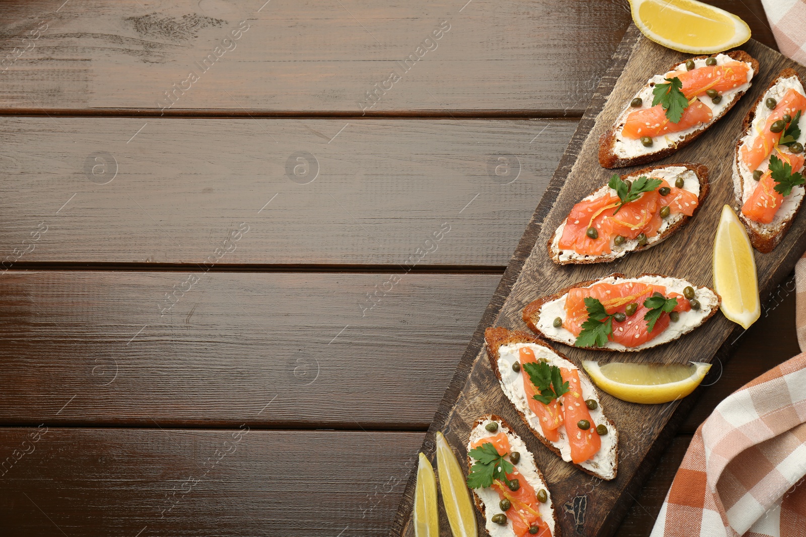 Photo of Tasty canapes with salmon, capers, lemon and cream cheese on wooden table, top view. Space for text