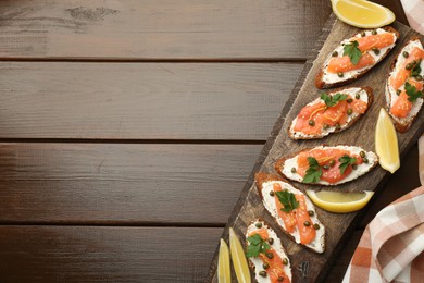 Photo of Tasty canapes with salmon, capers, lemon and cream cheese on wooden table, top view. Space for text