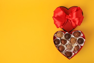 Photo of Heart shaped box with delicious chocolate candies on yellow background, flat lay. Space for text