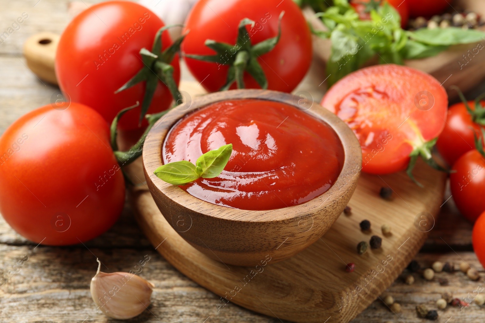 Photo of Tasty ketchup, fresh tomatoes, basil and spices on wooden table