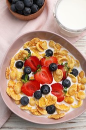 Photo of Bowl of tasty crispy corn flakes with milk and berries on white wooden table, flat lay