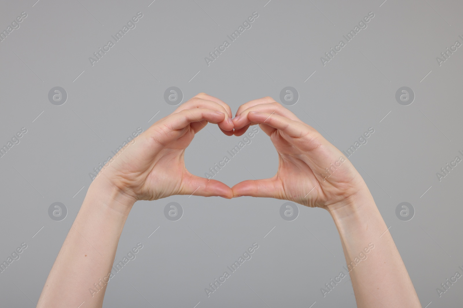 Photo of Woman showing heart gesture with hands on grey background, closeup