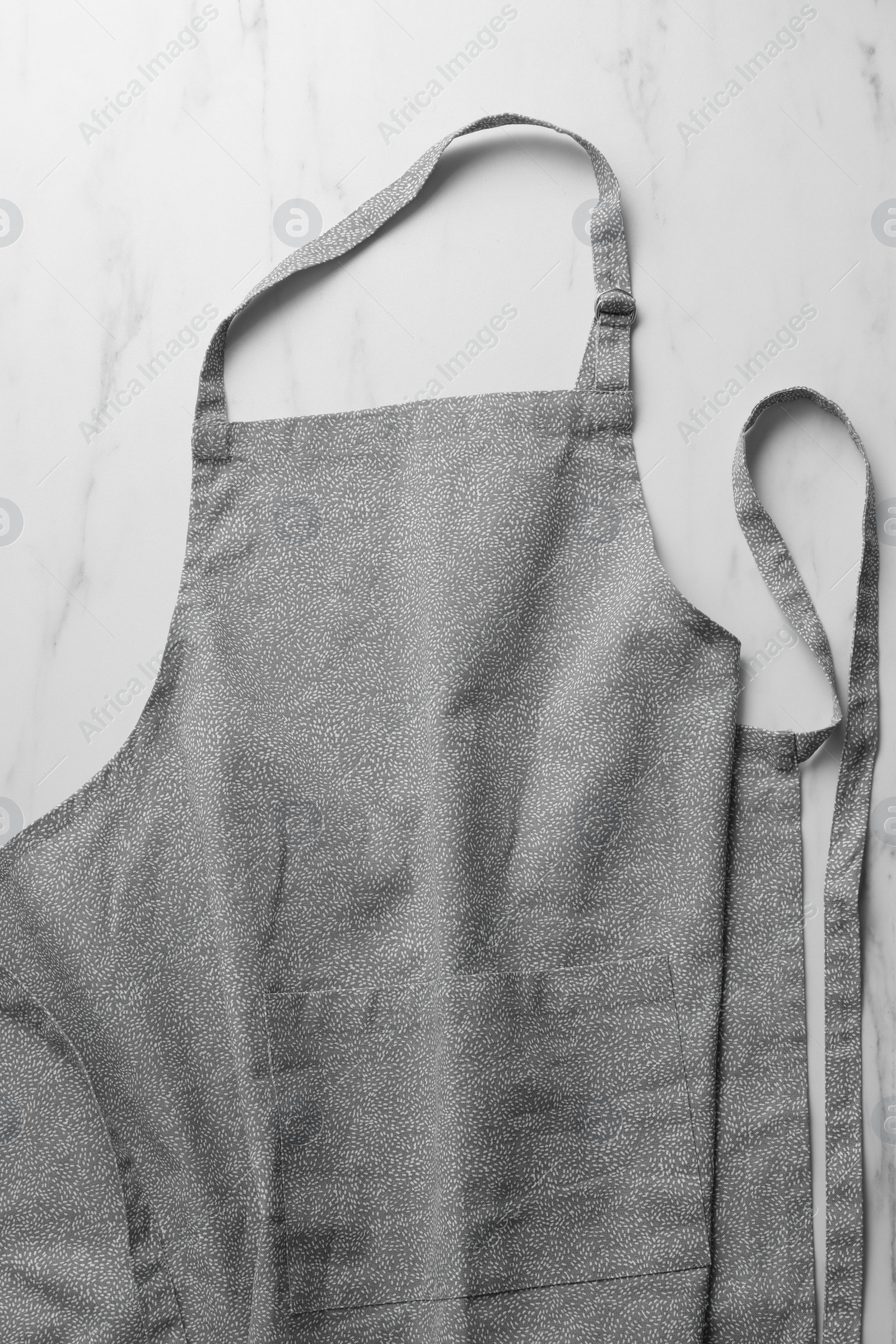 Photo of Grey apron with pattern on white marble table, top view