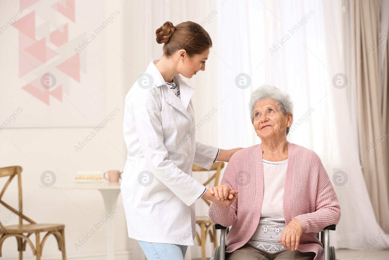 Photo of Nurse assisting elderly woman in wheelchair indoors