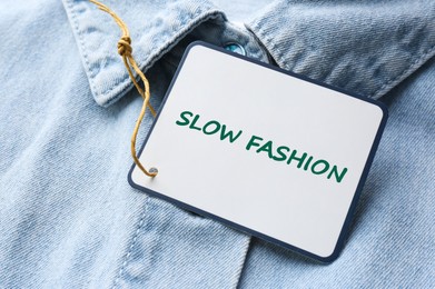 Image of Conscious consumption. Tag with words Slow Fashion on denim shirt, closeup