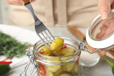 Photo of Woman taking pickled cucumber from jar at table, closeup view