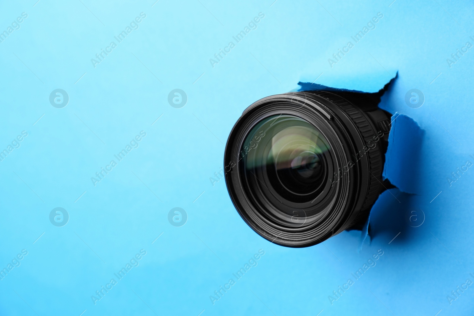 Photo of Hidden camera lens through torn hole in light blue paper. Space for text