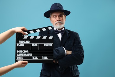 Photo of Senior actor performing role while second assistant camera holding clapperboard on light blue background. Film industry