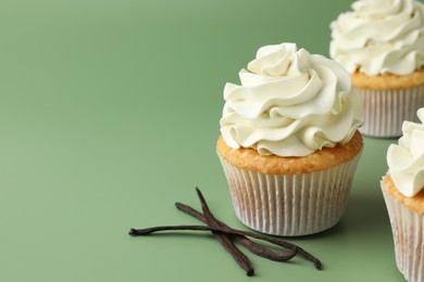 Tasty cupcakes with cream and vanilla pods on green background, closeup. Space for text