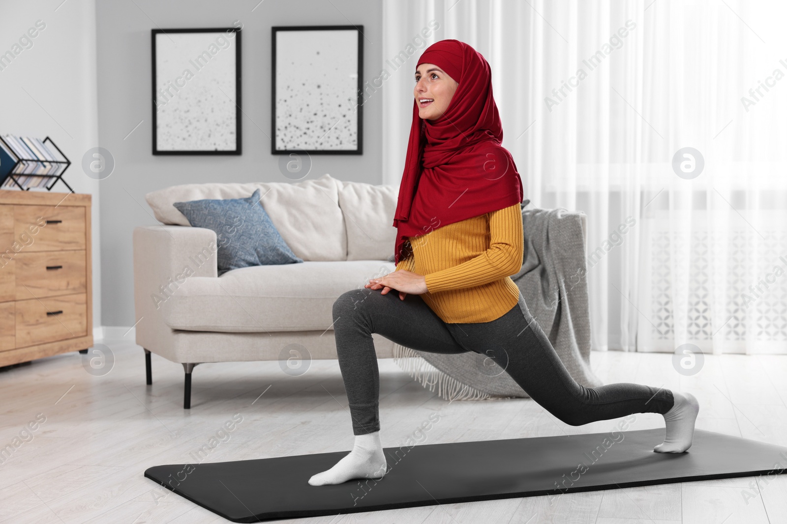 Photo of Muslim woman in hijab stretching on fitness mat at home. Space for text