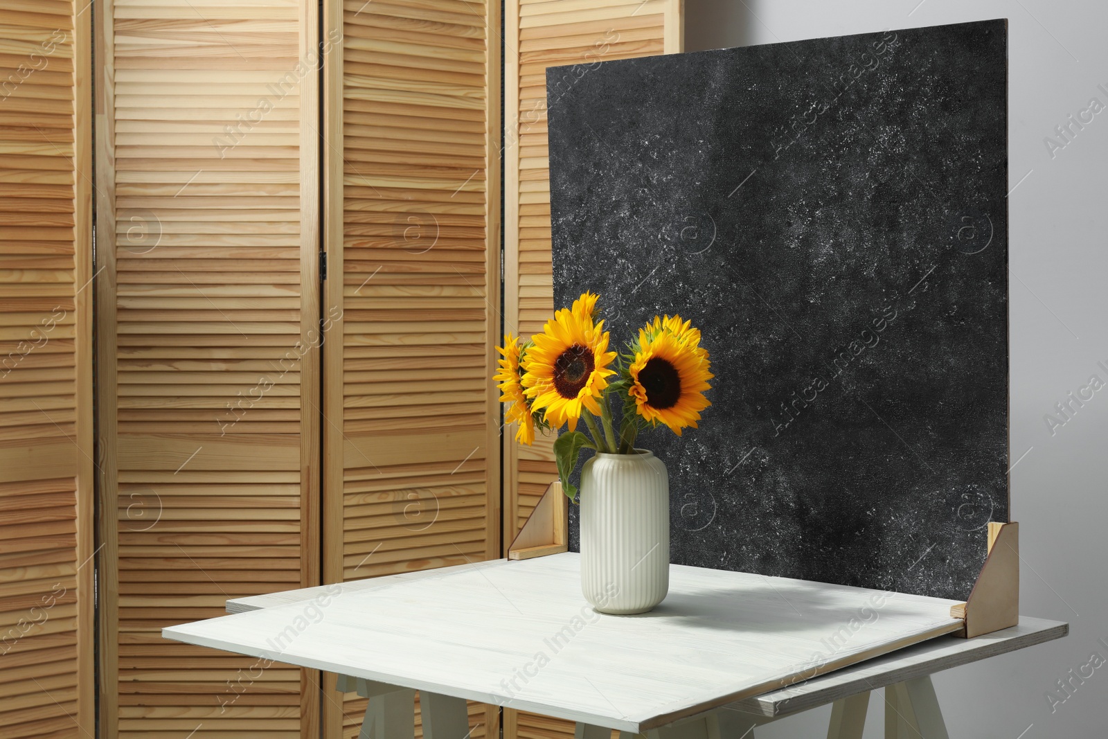 Photo of Vase with beautiful sunflowers and double-sided backdrop on table in photo studio