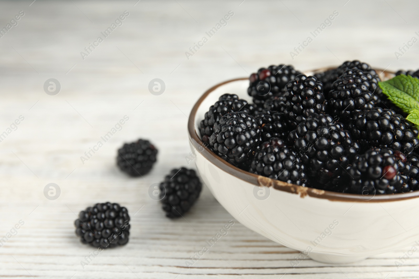 Photo of Bowl of ripe blackberries with mint on white wooden table, closeup