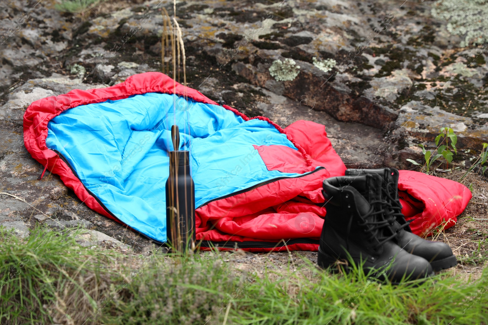 Photo of Sleeping bag, boots and bottle outdoors. Camping gear