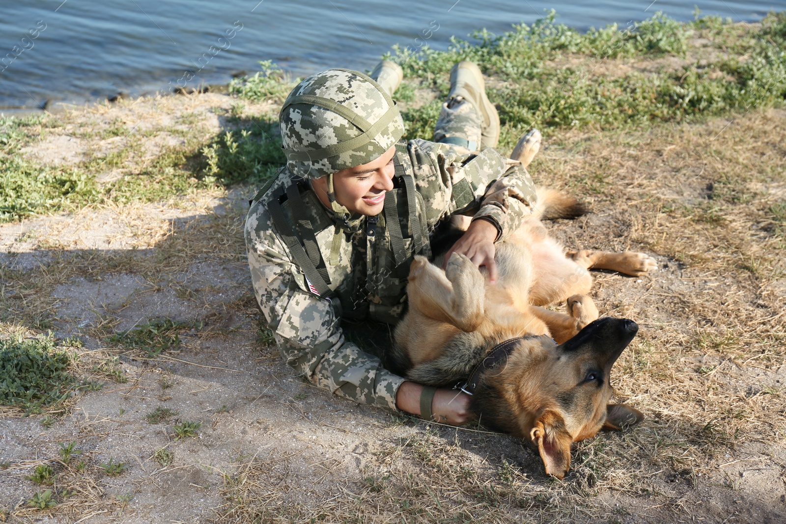 Photo of Man in military uniform with German shepherd dog near river