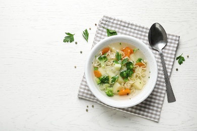 Bowl of fresh homemade vegetable soup served on white wooden table, flat lay. Space for text