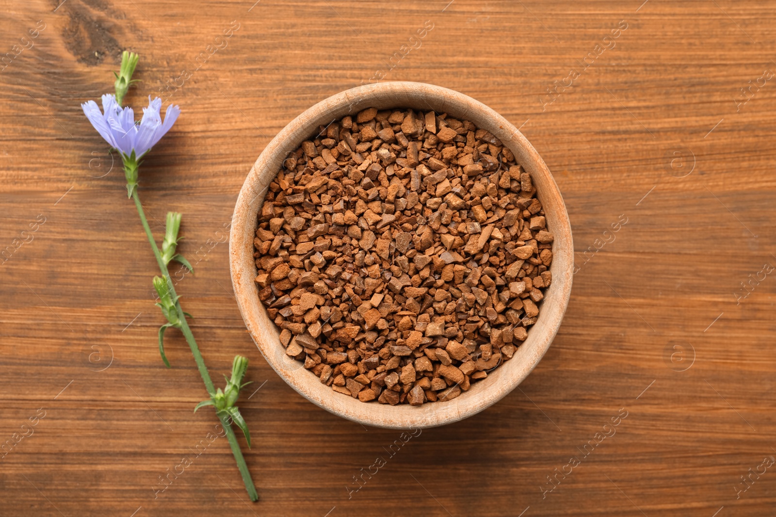 Photo of Bowl of chicory granules and flower on wooden table, flat lay