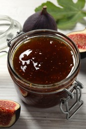 Glass jar with tasty sweet jam and fresh figs on white table, closeup