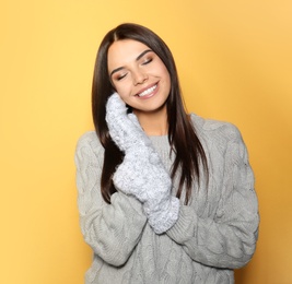 Image of Happy young woman wearing warm sweater and mittens on yellow background 