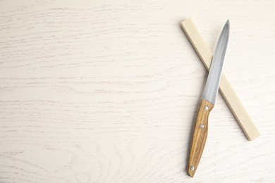 Photo of Sharpening stone and knife on white wooden table, flat lay. Space for text
