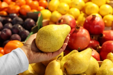 Photo of Woman holding fresh pear near fruit counter at market, closeup