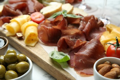 Photo of Charcuterie board. Delicious bresaola, olives, tomato, cheese and almond on table, closeup