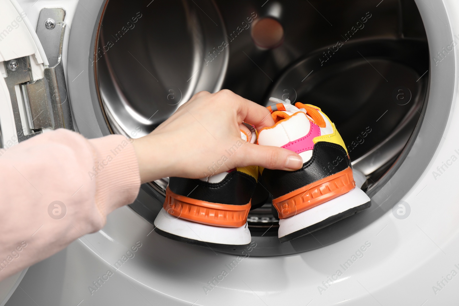 Photo of Woman putting stylish sneakers into washing machine, closeup