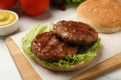 Delicious fried patties, lettuce and bun on white table, closeup. Making hamburger