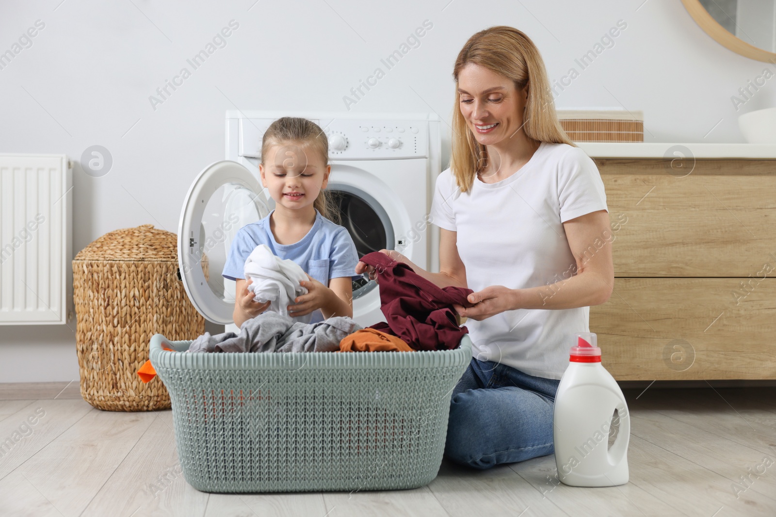 Photo of Mother and daughter taking out dirty clothes from basket in bathroom