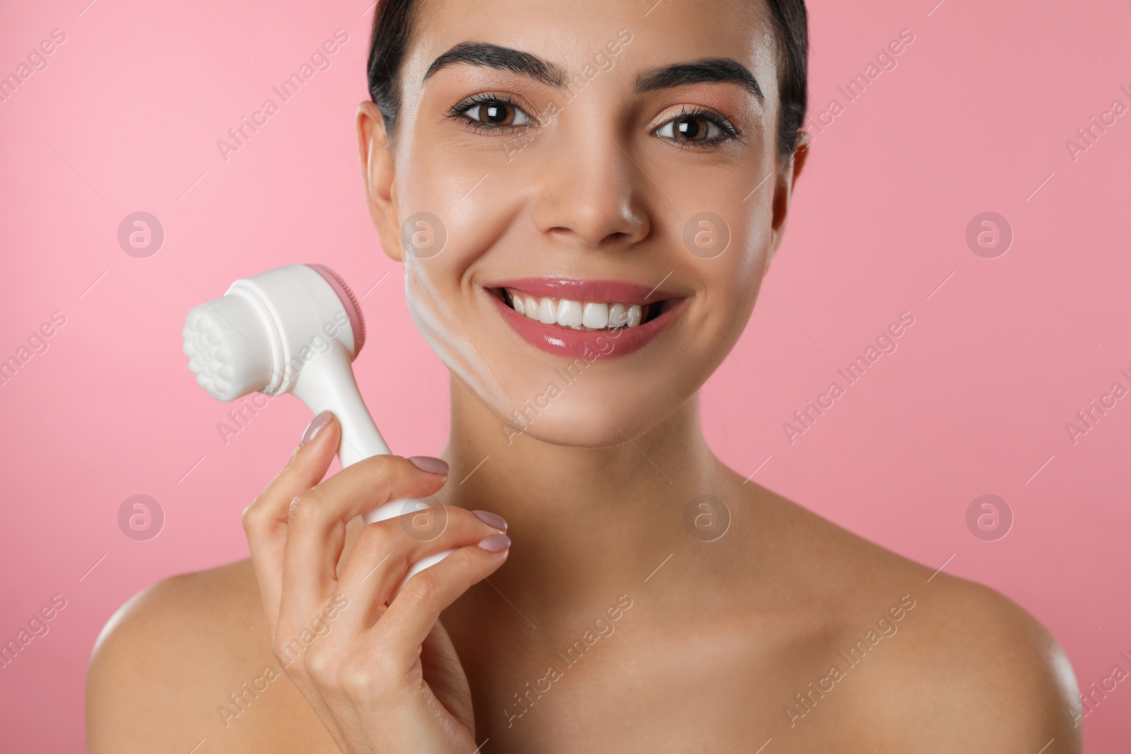 Photo of Young woman holding facial cleansing brush on pink background, closeup. Washing accessory