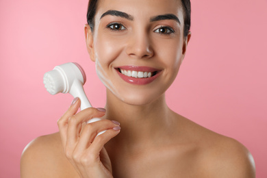 Photo of Young woman holding facial cleansing brush on pink background, closeup. Washing accessory