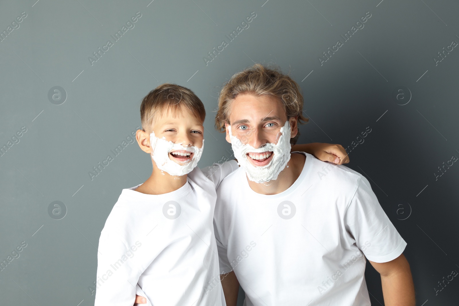 Photo of Father and son with shaving foam on faces against color background