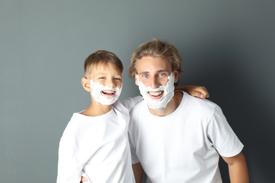 Photo of Father and son with shaving foam on faces against color background