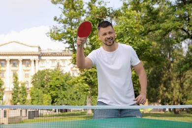 Happy man playing ping pong outdoors on summer day
