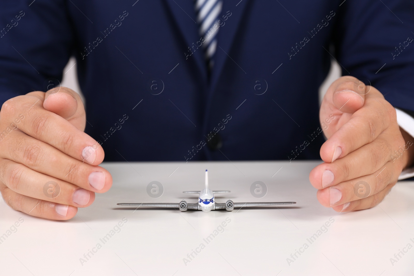 Photo of Insurance agent covering toy plane at table, closeup. Travel safety concept