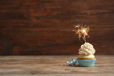 Photo of Birthday cupcake with sparkler on wooden table. Space for text