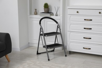 Photo of Metal folding ladder near chest of drawers and shelf with accessories in room