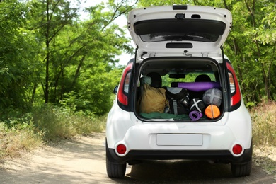 Photo of Car with camping equipment in trunk on forest road. Space for text