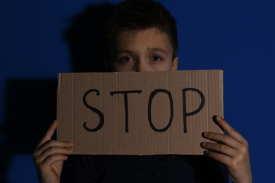 Abused little boy with sign STOP near blue wall. Domestic violence concept