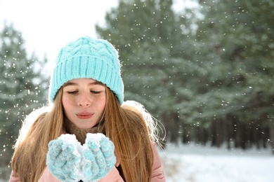 Teenage girl blowing snow in winter forest. Space for text