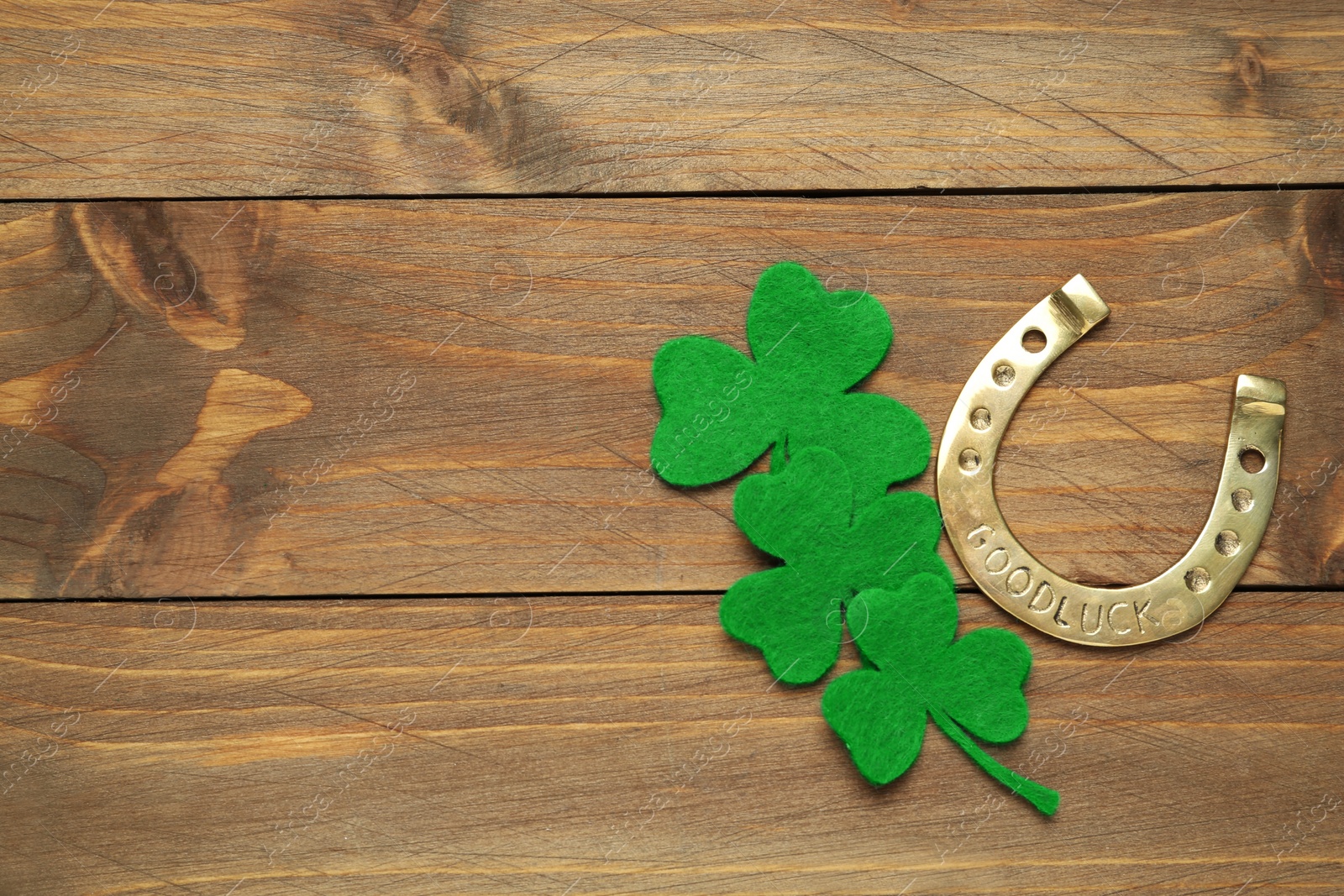 Photo of Decorative clover leaves and horseshoe on wooden background, flat lay with space for text. St. Patrick's Day celebration