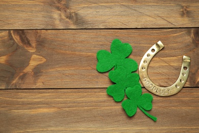 Decorative clover leaves and horseshoe on wooden background, flat lay with space for text. St. Patrick's Day celebration