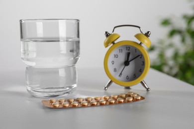Oral contraceptive pills, glass of water and alarm clock on white table