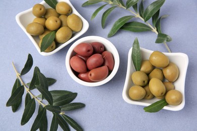 Photo of Different fresh olives and leaves on violet background, flat lay