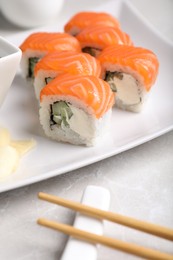 Photo of Tasty sushi rolls, ginger and chopsticks on grey table, closeup