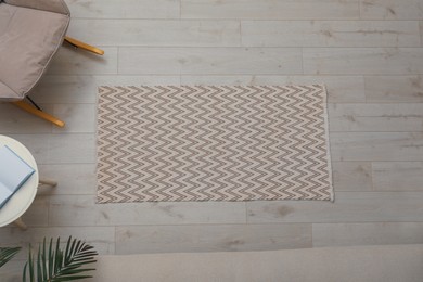 Light carpet with geometric pattern on wooden floor in room, top view